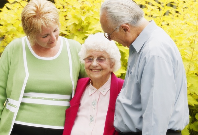 an elderly woman in a pink jacket is surrounded by a man and woman