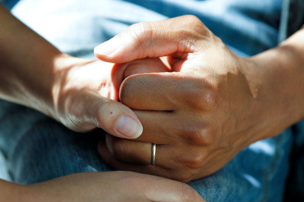 a woman wearing a wedding ring holds another woman 's hand