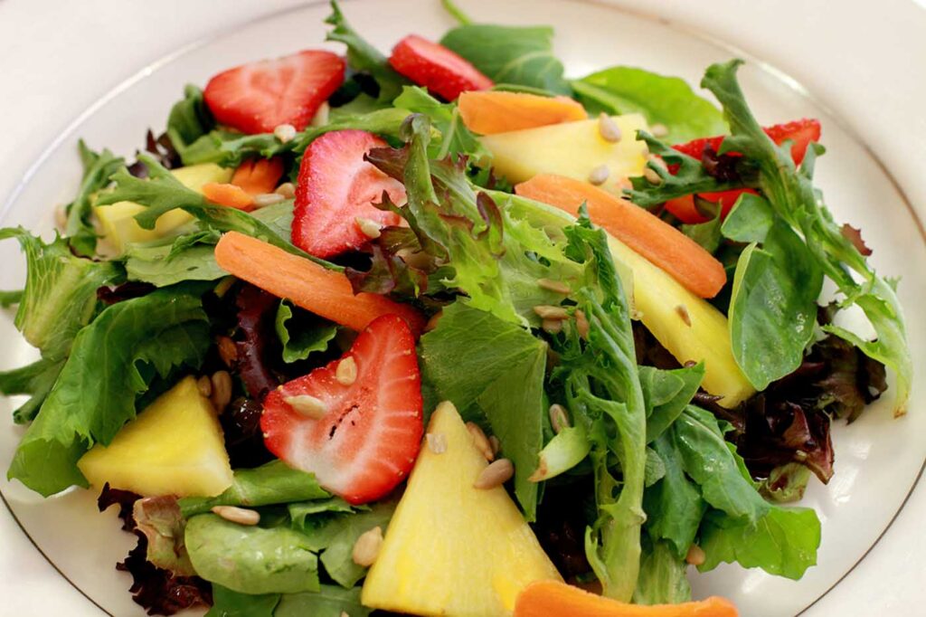 a salad with strawberries, pineapple, and carrots on a white plate