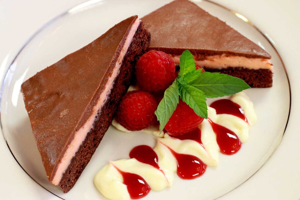 a chocolate cake with raspberries and whipped cream on a white plate