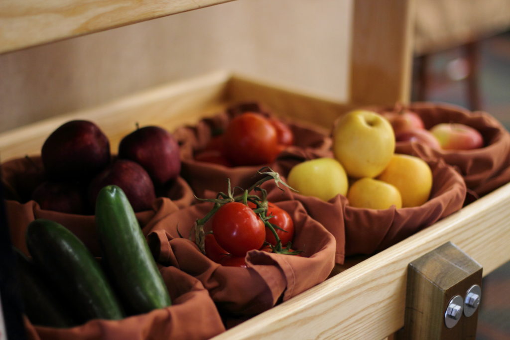 a display of fruits and vegetables including tomatoes, apples, and cucumbers