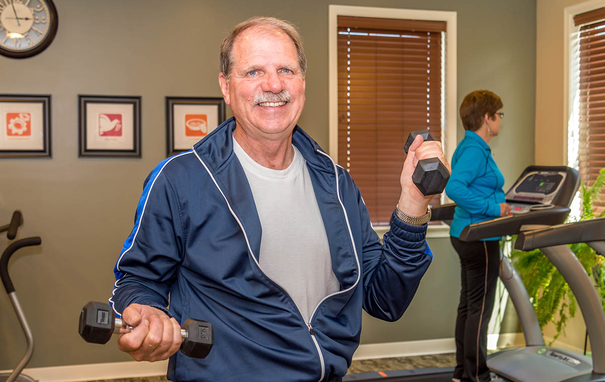 a man in his 60s holding a dumbbell in a gym
