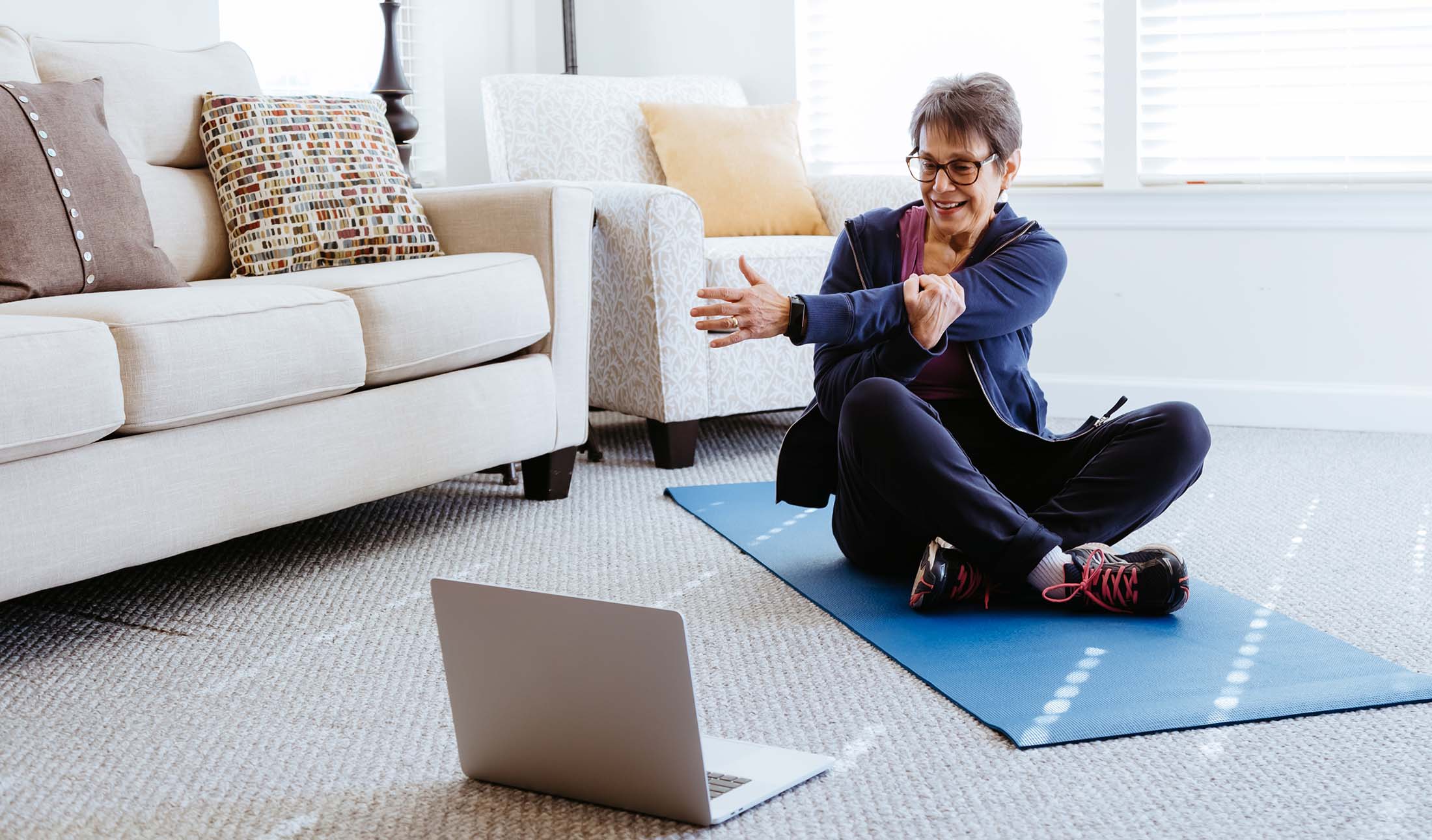 a woman sits on a yoga mat in front of a laptop