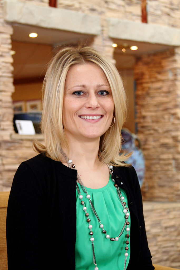 a woman wearing a green shirt and a black cardigan smiles for the camera