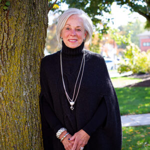 Mary leans up against a tree while wearing silver jewelry