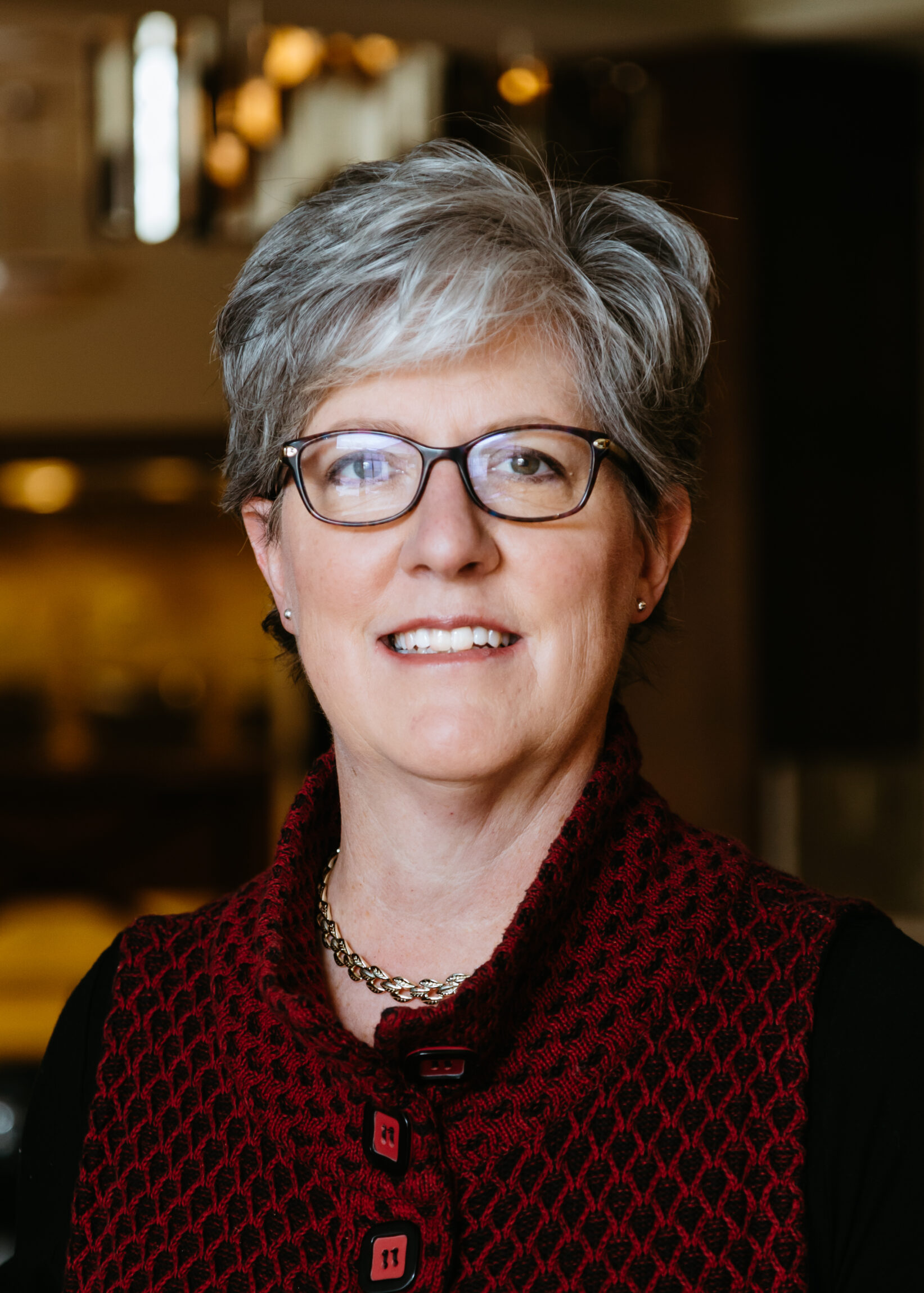 A headshot of a woman with grey hair wearing glasses