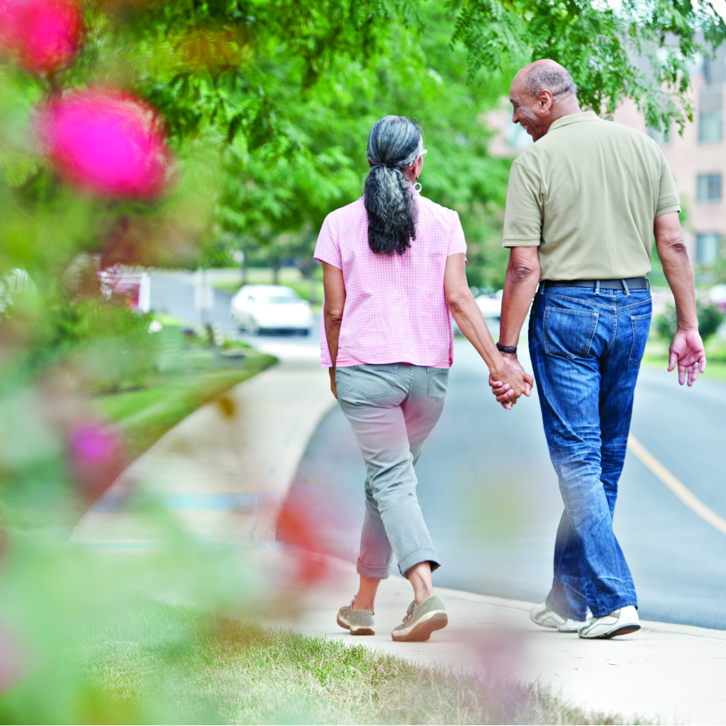 An elderly couple holds hands while walking around outside