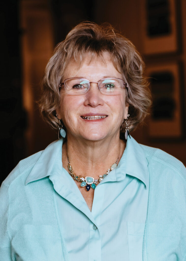 a woman wearing glasses and a necklace smiles for the camera
