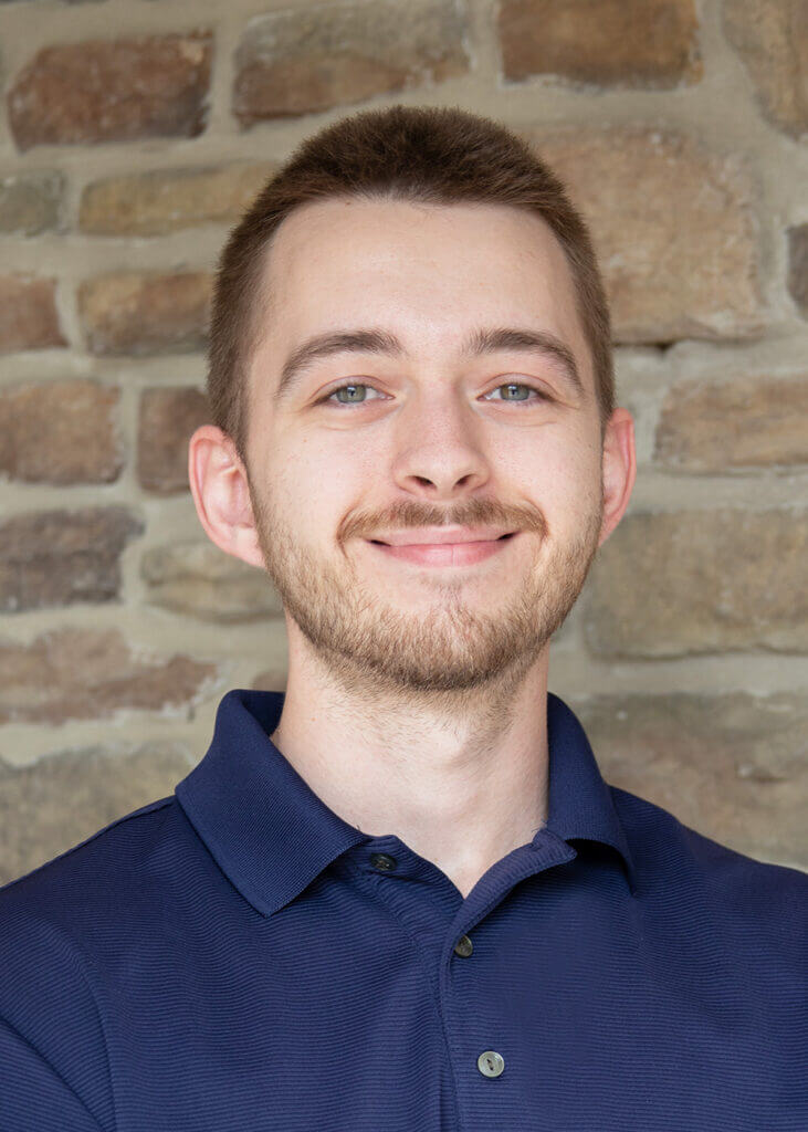 a man with a beard is smiling in front of a stone wall