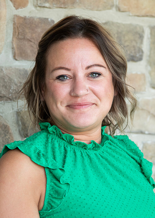 a woman wearing a green top is smiling in front of a stone wall