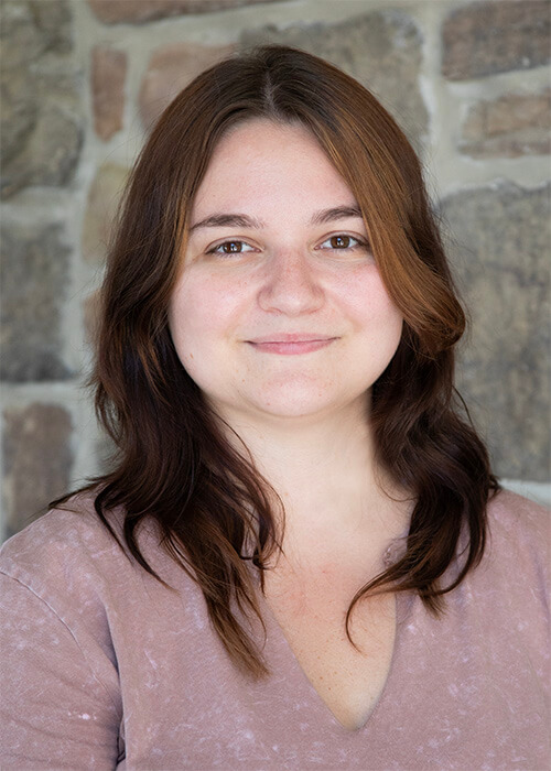 a woman with long brown hair is smiling in front of a stone wall