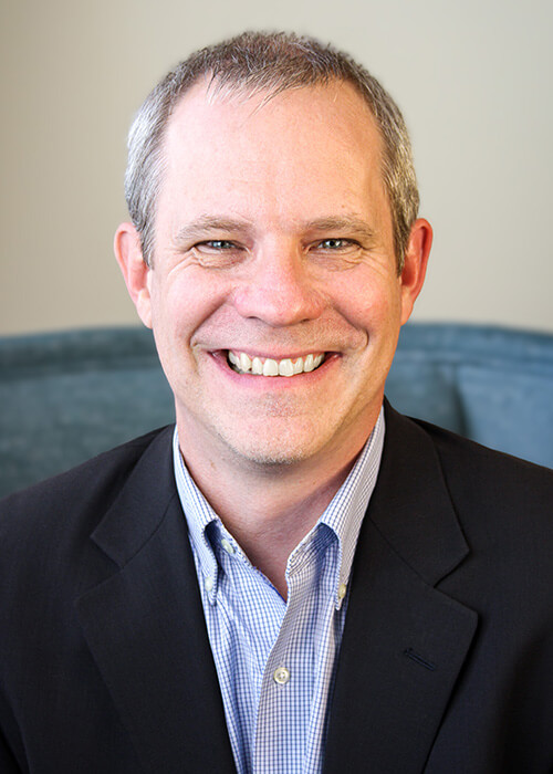 a man in a suit and plaid shirt smiles for the camera